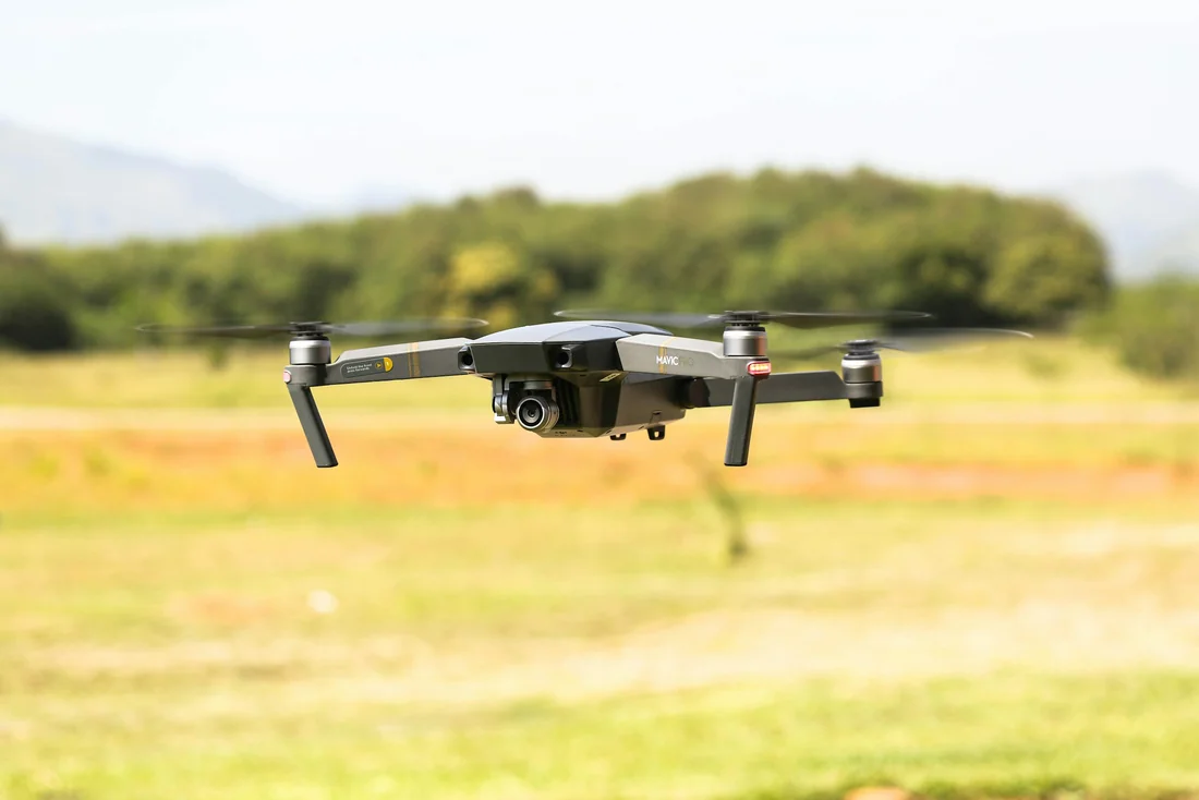 Consumer quadcopter in flight above a grassy open area.