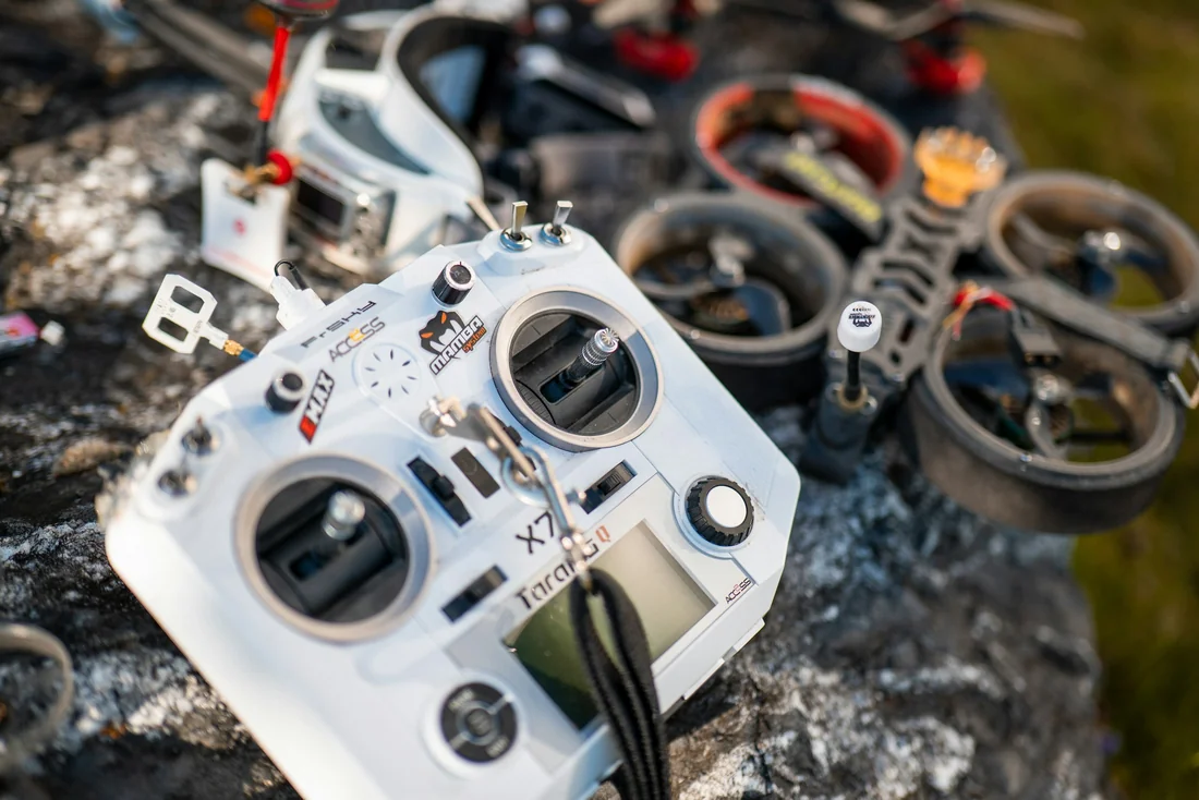 Radio transmitter and FPV quadcopter resting on a rock outdoors